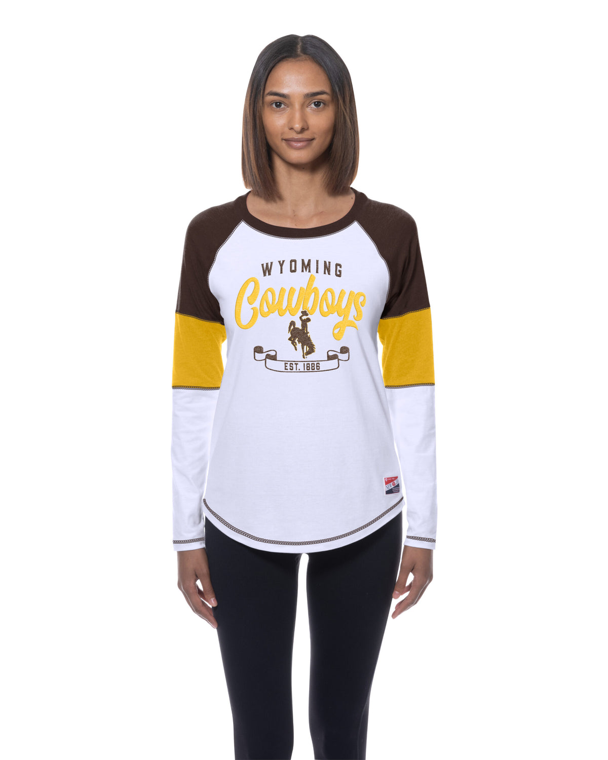 model wearing a long sleeve with brown, gold and white panels on sleeves. has wyoming lettering with cowboys script and bucking horse with est. 1886 below all center chest