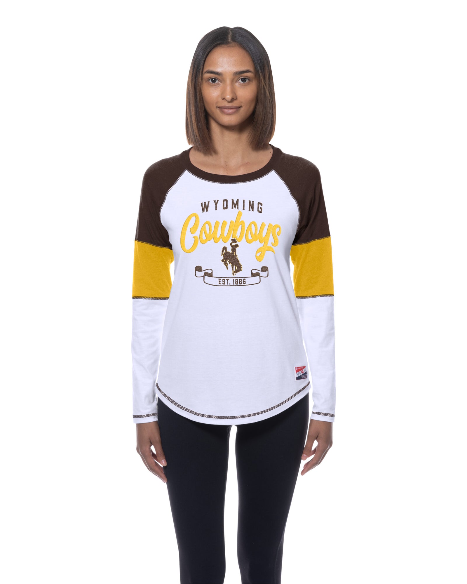 model wearing a long sleeve with brown, gold and white panels on sleeves. has wyoming lettering with cowboys script and bucking horse with est. 1886 below all center chest