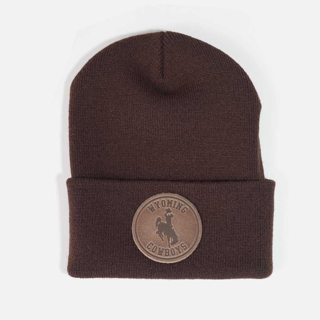 Brown beanie, design is brown leather patch with word Wyoming above bucking horse above cowboys