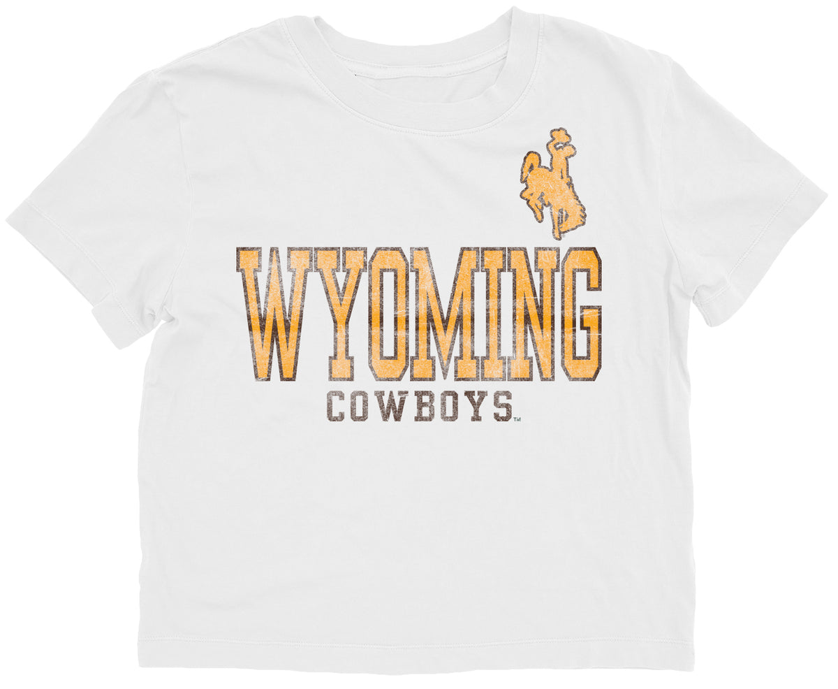 White short sleeve tee. Design is front center chest. Wyoming in gold with brown outline with cowboys in brown under. gold bucking horse left upper chest