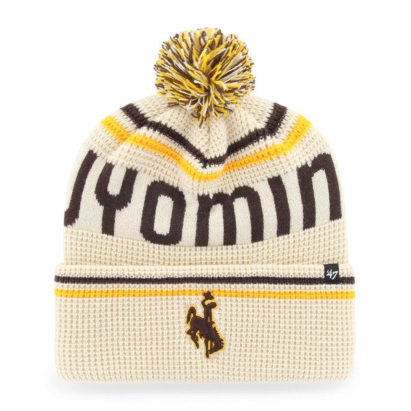 A cream-colored knit beanie with a yellow and brown pom-pom, featuring the word 'Wyoming' in dark brown across the top, yellow and brown stripes, a small embroidered bucking horse logo, and a '47 brand tag on the cuff.