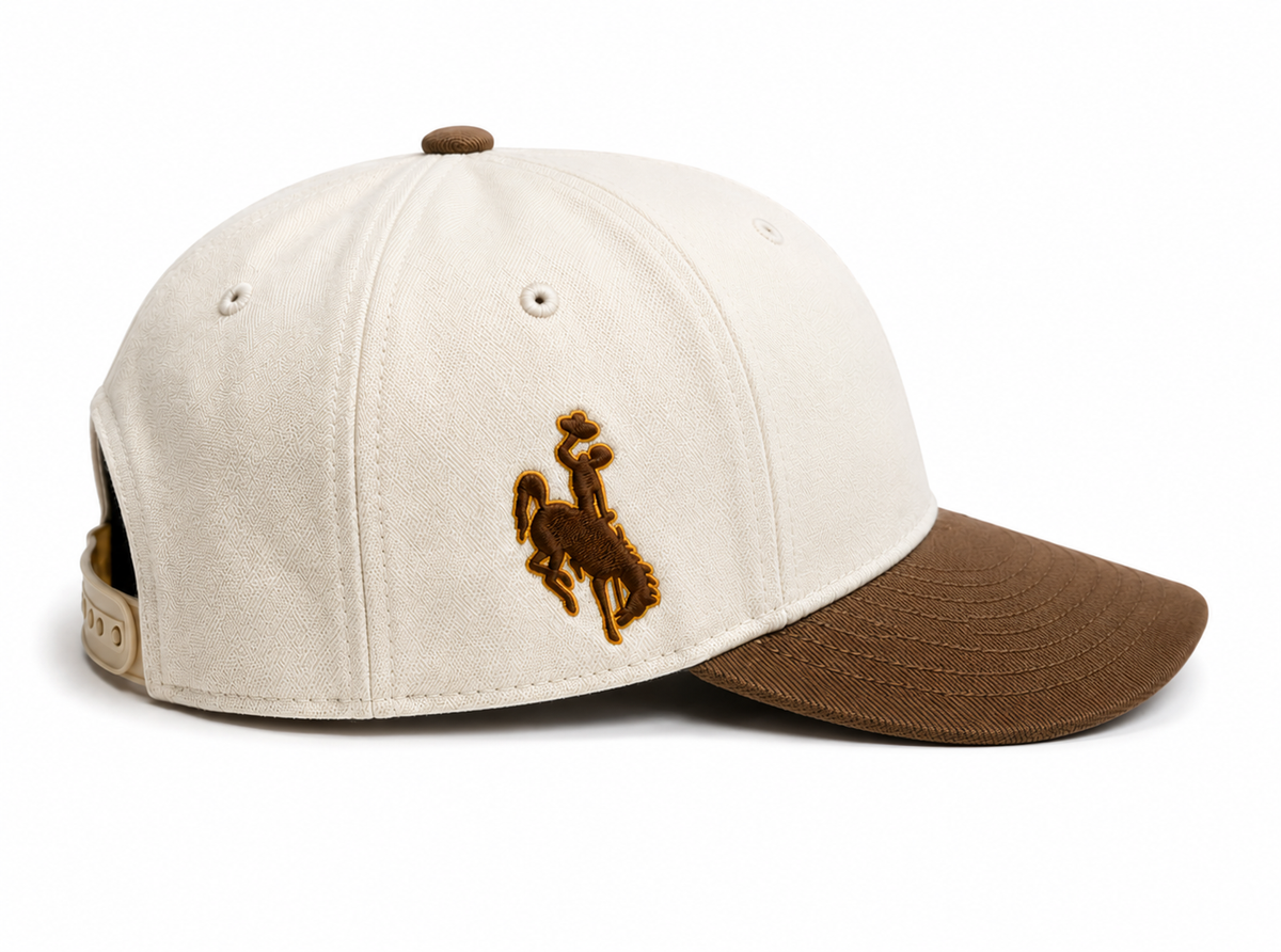 Cream and brown hat pictured from the side. Has brown bucking horse embroidered. Pictured on a white background.