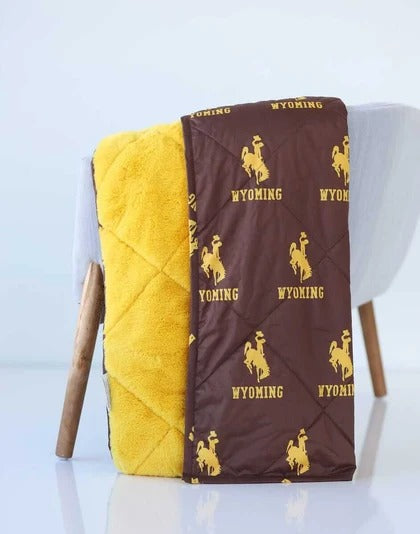Brown and gold minky everywhere blanket. has wyoming and bucking horse logo on brown side and other side is gold plush. Pictured hanging on side of the chair and has a white background.