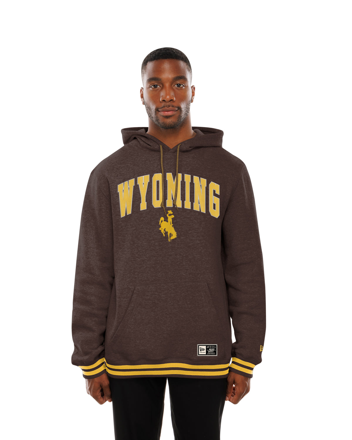 Man modeling a brown hooded sweatshirt with wyoming and bucking horse logo on front and has gold pin stripes on waist band and wrist cuffs. Pictured on a white background.