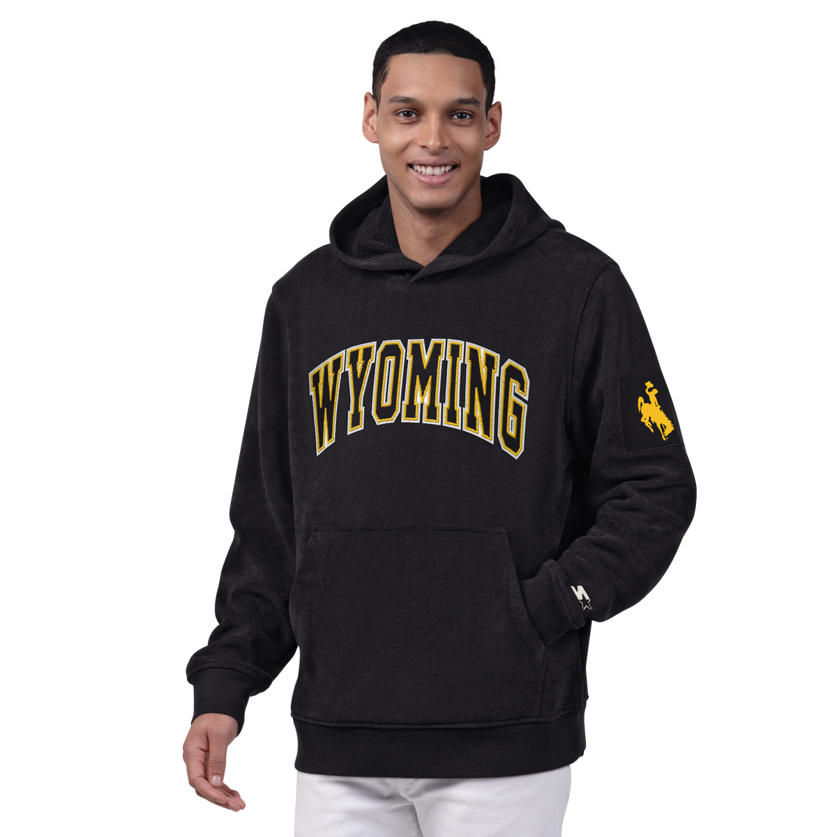Man wearing black hooded sweatshirt with wyoming lettering on the front and gold bucking horse logo on the left sleeve. Pictured on a white background.
