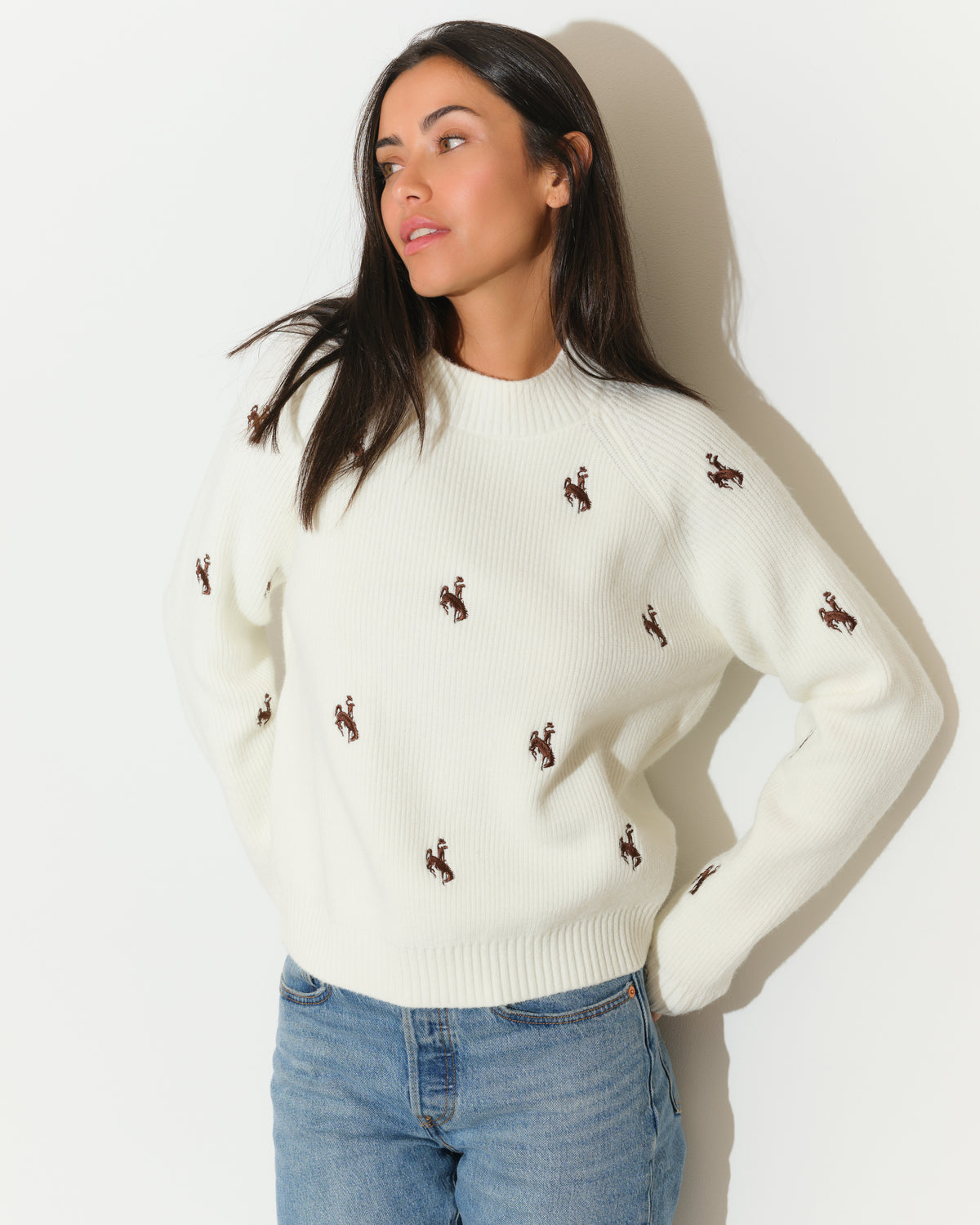 Women modeling ivory sweater with brown bucking horse logos all over it. Pictured on a white background.