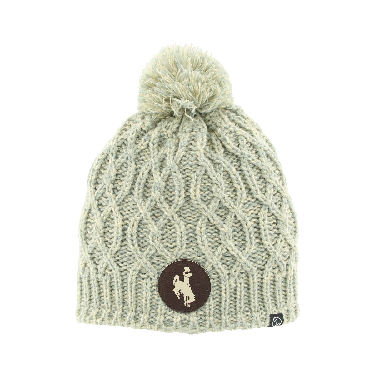 A cream cable-knit beanie hat with a matching pom-pom on top and a circular brown logo patch on the front.