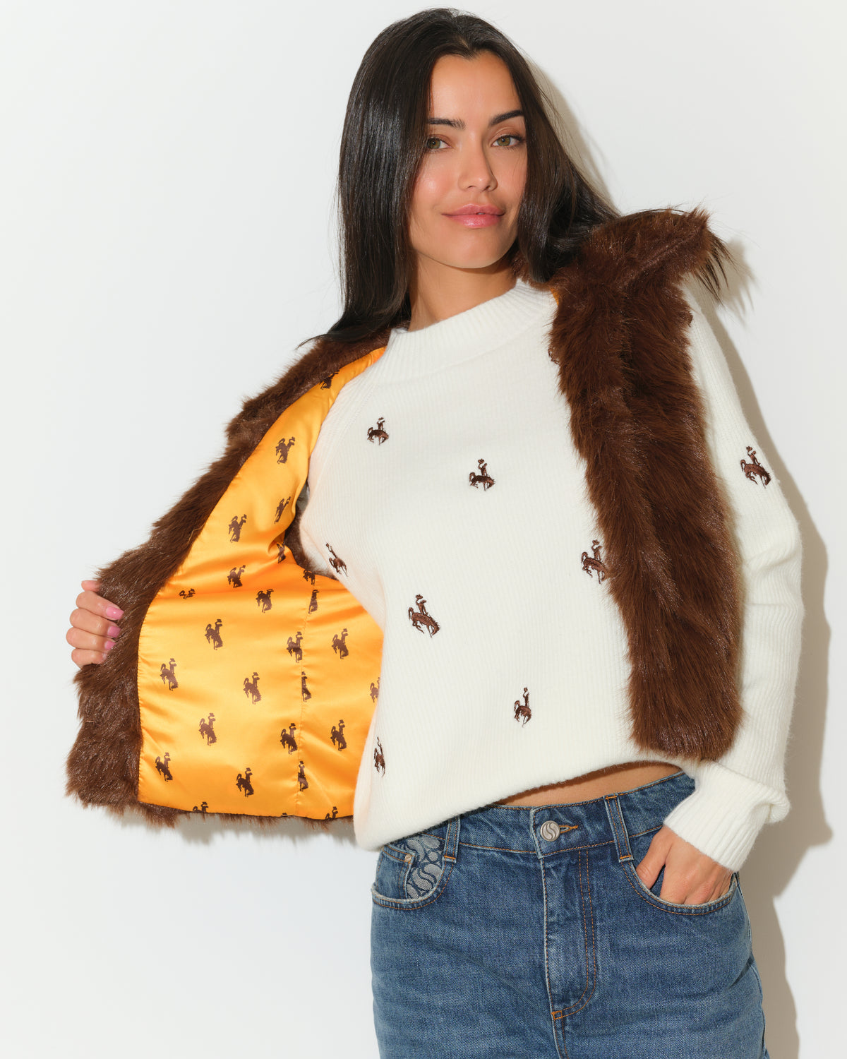 Women wearing a ivory sweater and brown faux vest to model. Vest has gold satin lining and little bucking horses logo all over it. Same with the sweater. Pictured on a white background.