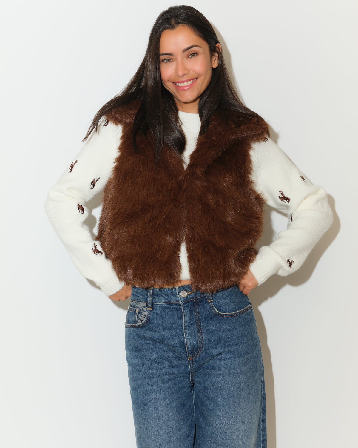 Women modeling brown fur vest with ivory sweater below and blue jeans. Showing how to style this vest.