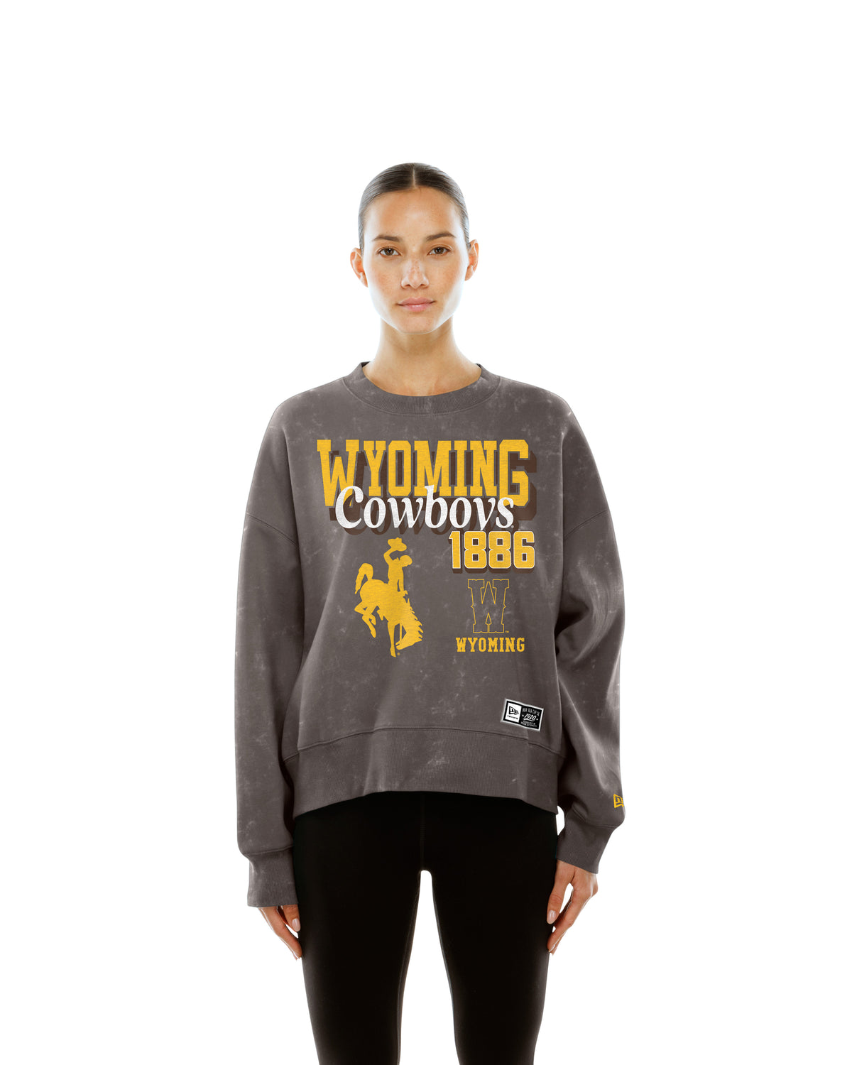 Woman wearing brown crewneck with full graphic on front. Says wyoming cowboys 1886 with bucking horse logo and W logo. Pictured on a white background.