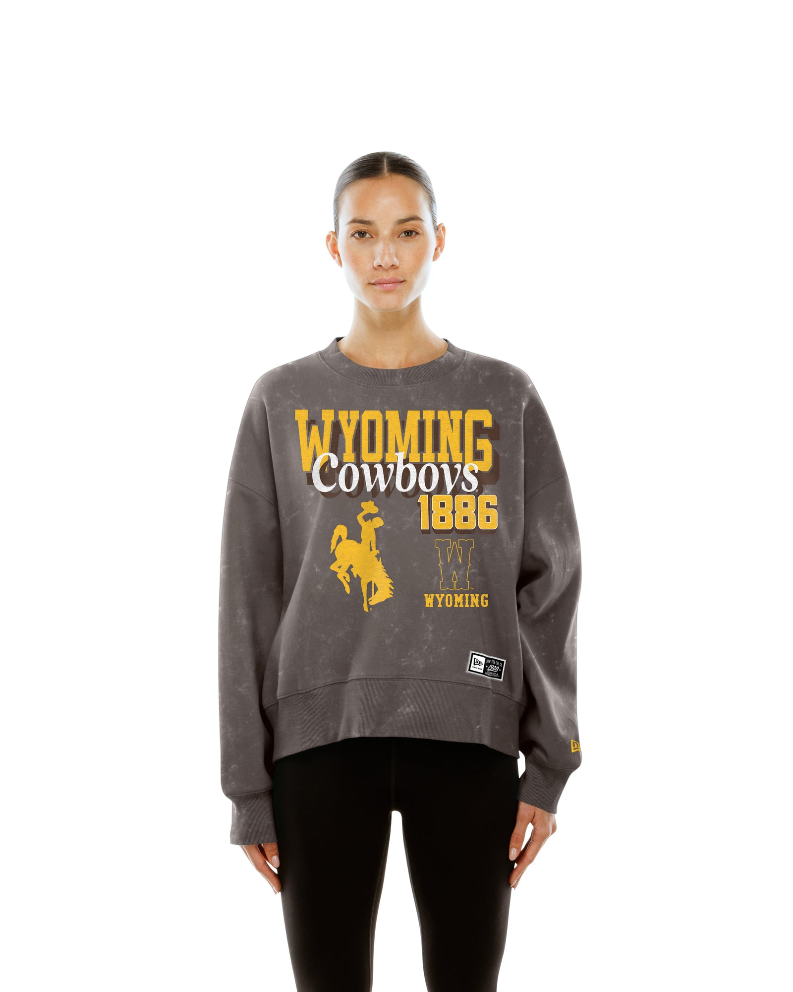 Woman wearing brown crewneck with full graphic on front. Says wyoming cowboys 1886 with bucking horse logo and W logo. Pictured on a white background.