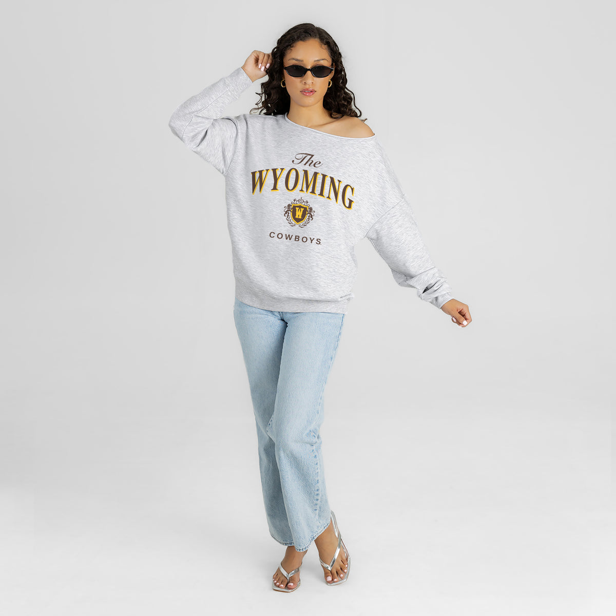 Woman wearing a gray 'The Wyoming Cowboys' sweatshirt and light blue jeans on a white background
