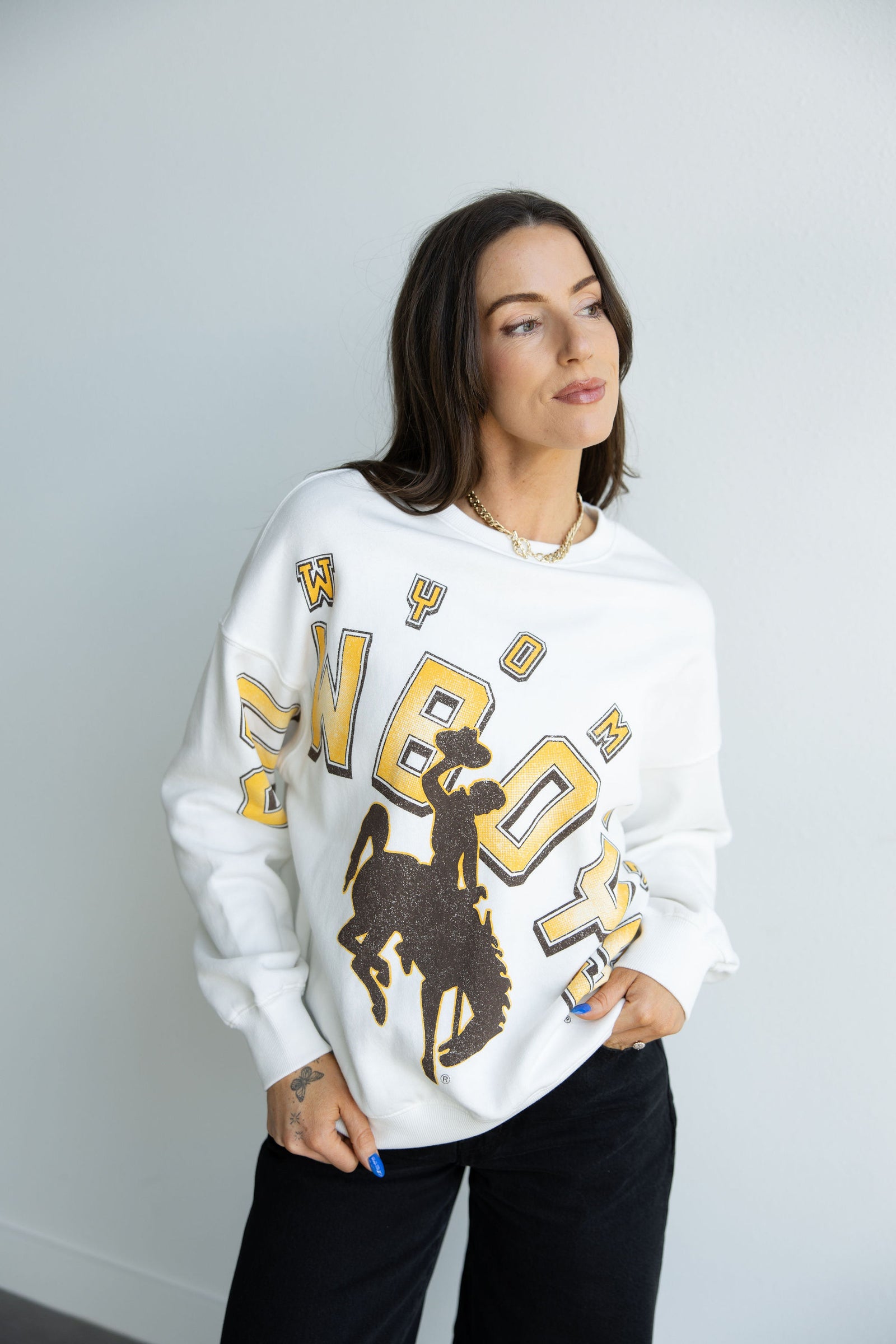 Woman wearing a white sweatshirt with 'Cowboys' and a oversized bucking horse logo on a plain background