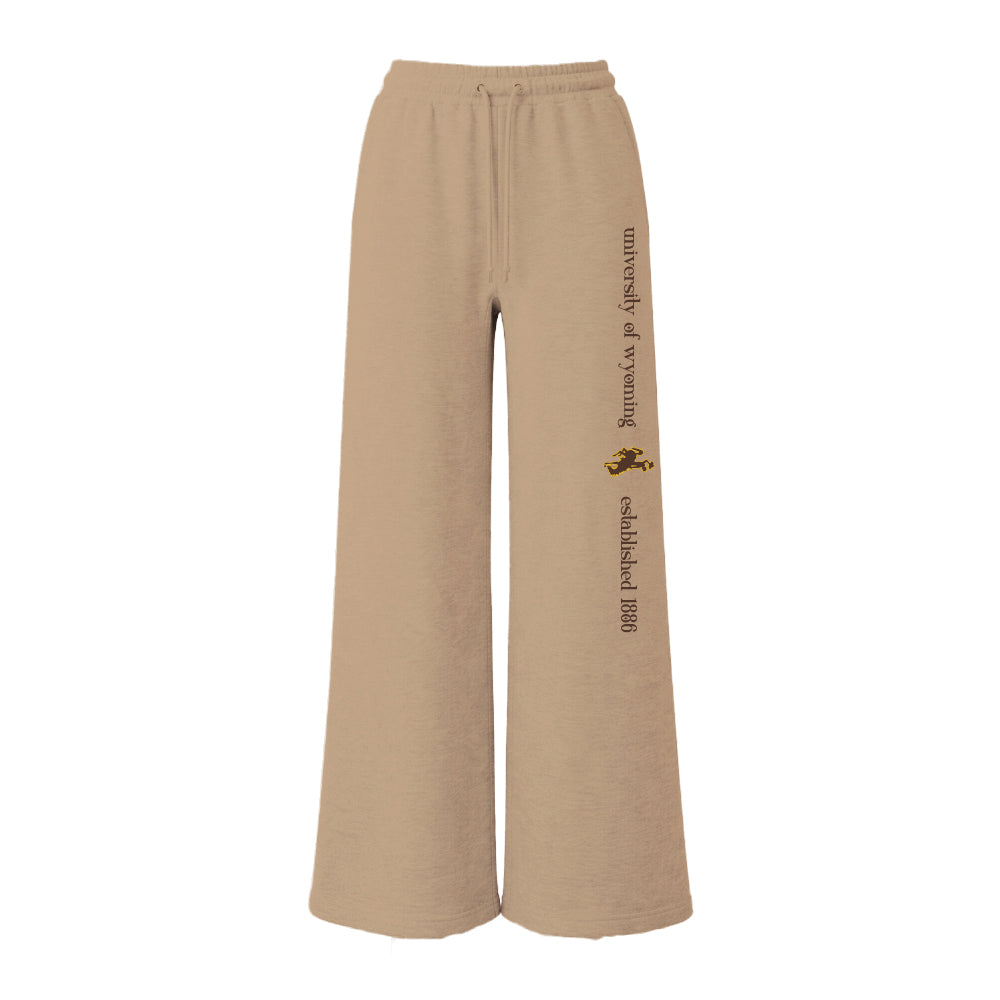 Tan women's wide leg pants with university of wyoming and bucking horse logo with established 1886 going down left leg. Pictured on a white background.
