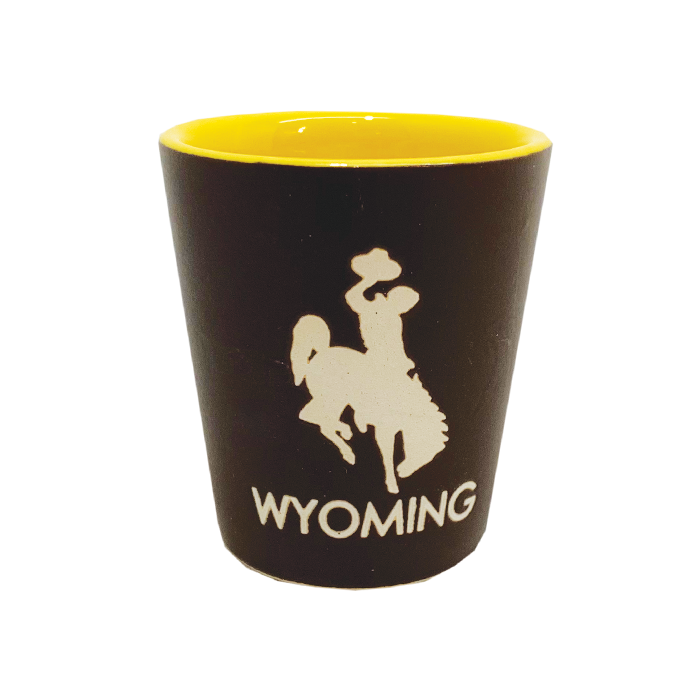 brown ceramic shot glass with gold on inside. large bucking horse and word Wyoming printed in white on front