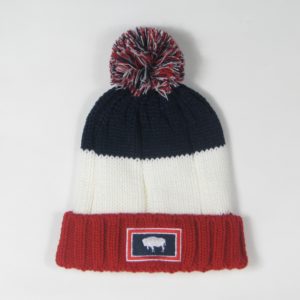 knit beanie made up of 3 striped color blocks, starting with red on bottom, white, and navy on top. multi colored pom. Wyoming state flag patch on front