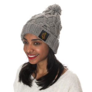chunky, grey cable knit beanie with cuff and pom on top. black rubberized patch with brown bucking horse sewn on the left side of front cuff.