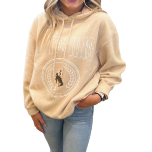 woman wearing oatmeal hooded sweatshirt, design on front center is word Wyoming in white, white seal with brown bucking horse inside