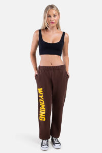woman wearing brown short sweatpants, design is vertical word Wyoming in gold on right leg