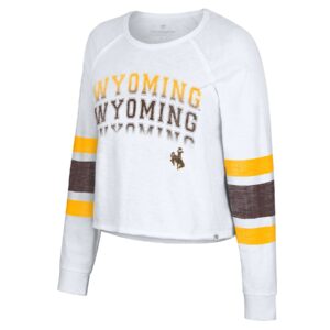 women's white long sleeve crop tee, gold and brown stripes on sleeves, design is word Wyoming repeated in gold fading to brown, brown bucking horse below