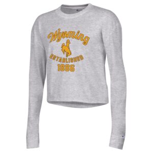 Women's grey cropped long sleeve, design is gold script word Wyoming above gold bucking horse, gold established 1886 below bucking horse