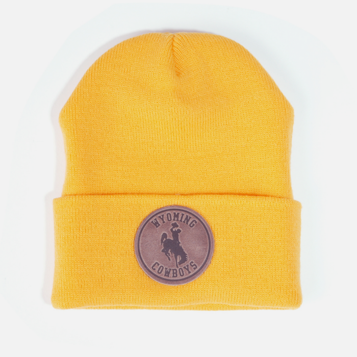 Gold beanie, design is brown leather patch with word Wyoming above bucking horse above cowboys