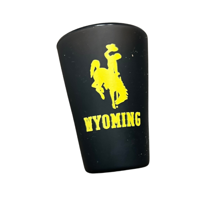 Black silicone shot glass, design is gold bucking horse above gold word Wyoming