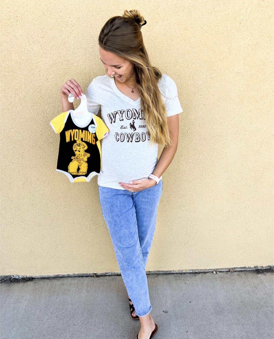 woman holding baby bump with a onesie in front of brown and gold