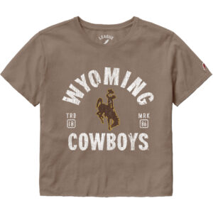 Light brown short sleeve crop t-shirt. Design is center chest, wyoming at top, arced, with brown bucking horse under. Cowboys at bottom of design. text is bold white.