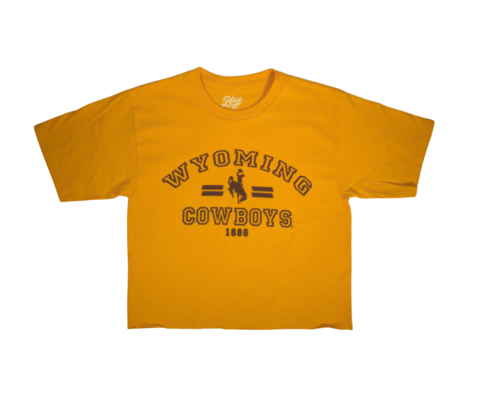 Gold short sleeve cropped tee with arced outline of wyoming with bucking horse and cowboys below. All text is brown.