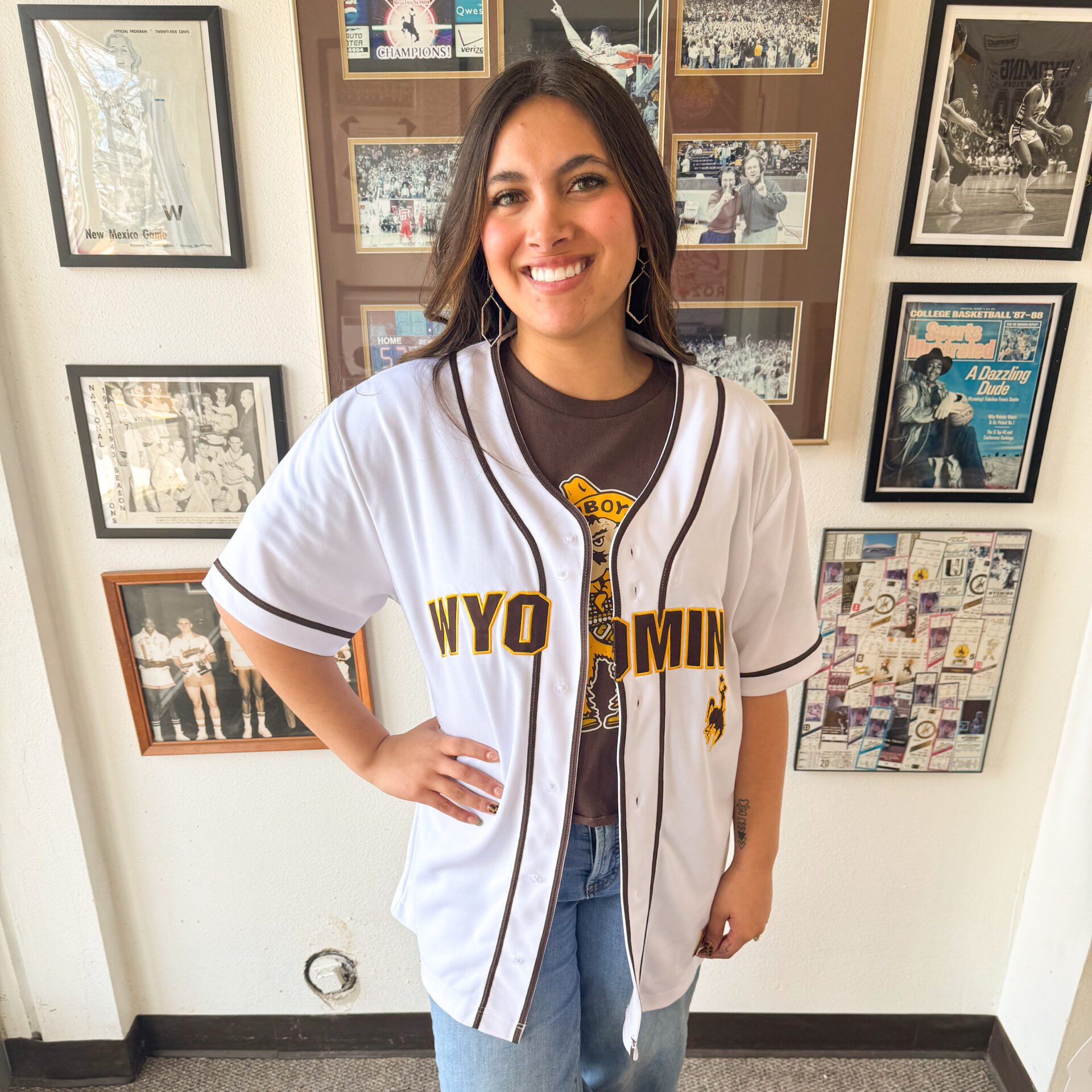 Employee wearing our new white baseball jersey is standing in front of a wall.