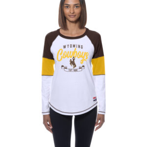 model wearing a long sleeve with brown, gold and white panels on sleeves. has wyoming lettering with cowboys script and bucking horse with est. 1886 below all center chest