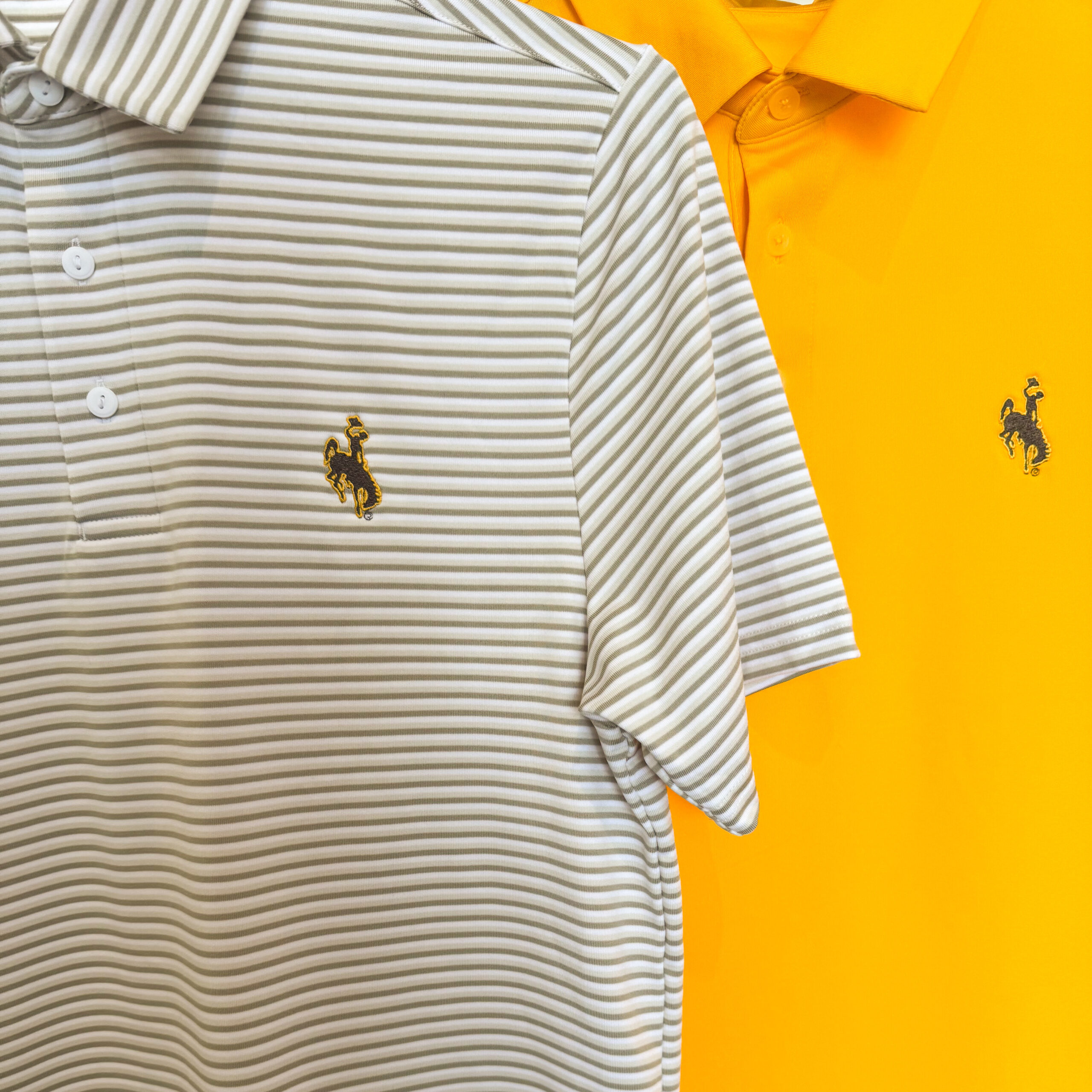 picture of two under armour polos. the one on the left is striped with embroidered bucking horse an the one on the right is gold with embroidered bucking horse