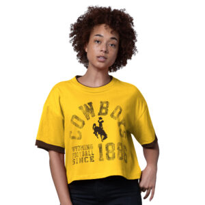 gold cropped tee shirt with brown outline on sleeves. has distressed logo on front with arched cowboys above bucking horse and has "wyoming football since 1886" below all