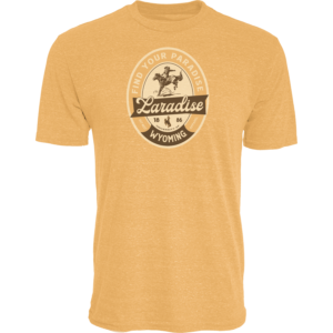 gold tee shirt with design center chest. design is an cream oval outline with cream "find your paradise" lettering around outside. has laradise script below with brown backround and wyoming lettering at bottom of oval. has old rider on bucking horse above laradise
